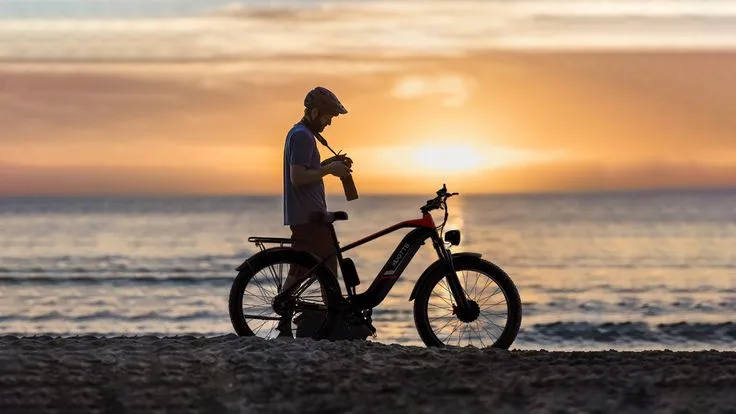 A man with his camera on an electric bike, with the sea and the sunset in the background